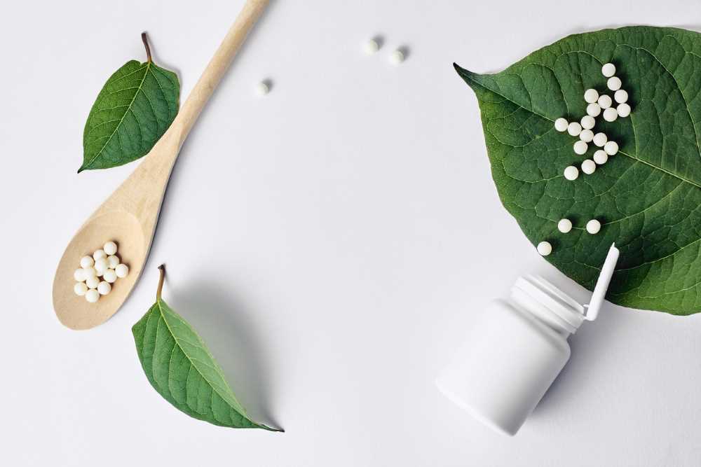 Homeopatika na stole, ležící na lžíci, ale i na listech. Velké množství kuliček homeopatik.
